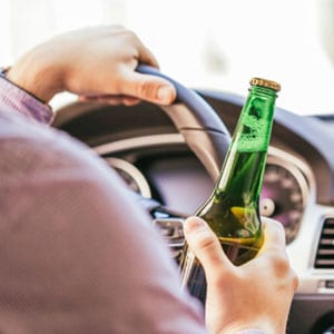 A man is driving with an alcohol in his hand - John Abel Law Office.