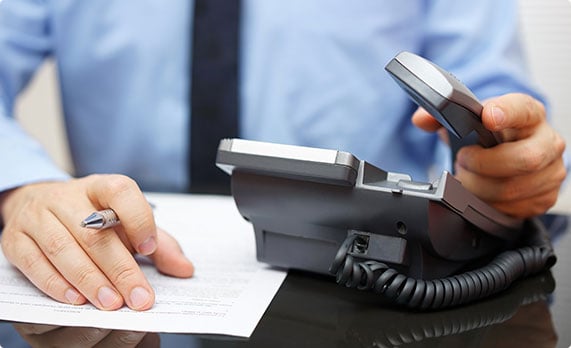 A man holding a phone in one hand and writing on a paper with the other hand - John Abel Law Office