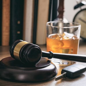 A gavel, a glass of alcohol, and a car key on a table, symbolizing DUI - John Abel Law Office