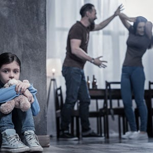 A young girl sits on the floor while her parents fight in the background, symbolizing domestic violence. - John Abel Law Office